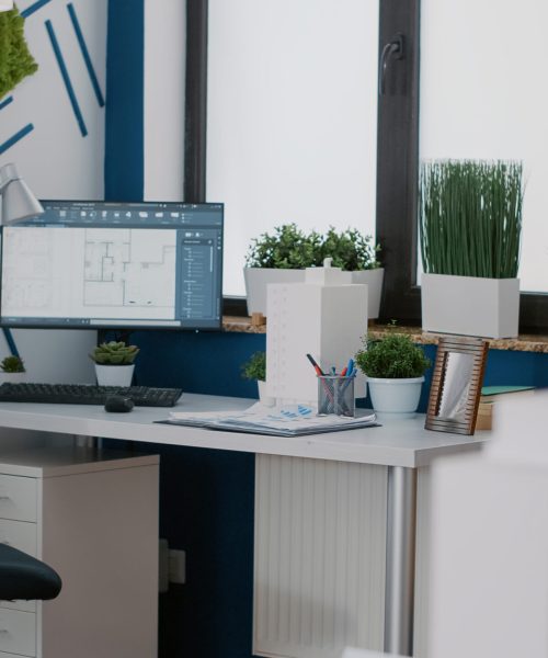 Close up of building model and maquette to design construction plan on table. Computer showing digital blueprints plans on computer monitor, used to create architectural presentation.